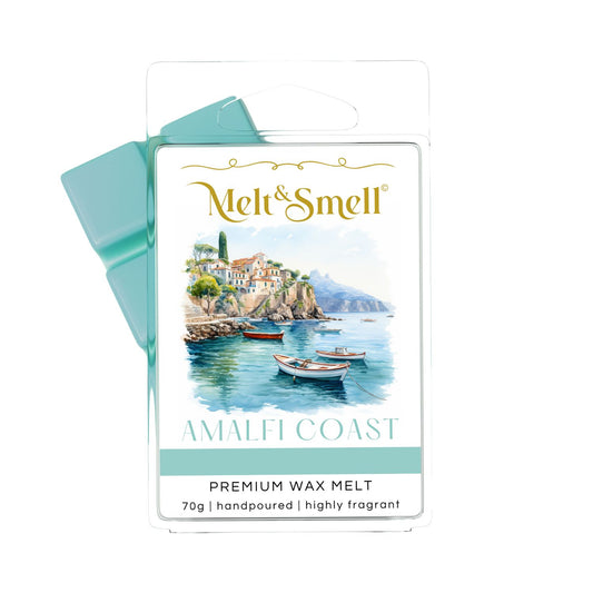 Eine Packung Melt & Smell Premium Duftwachs WAx Melt mit der Aufschrift „AMALFI COAST“. Die Verpackung zeigt eine idyllische Aquarellszene der Amalfiküste mit weißen Gebäuden, die an einer Klippe liegen, und mehreren kleinen Booten im blauen Wasser davor. Der Duftwachs selbst, das oben links aus der Verpackung herausragt, ist türkisfarben.